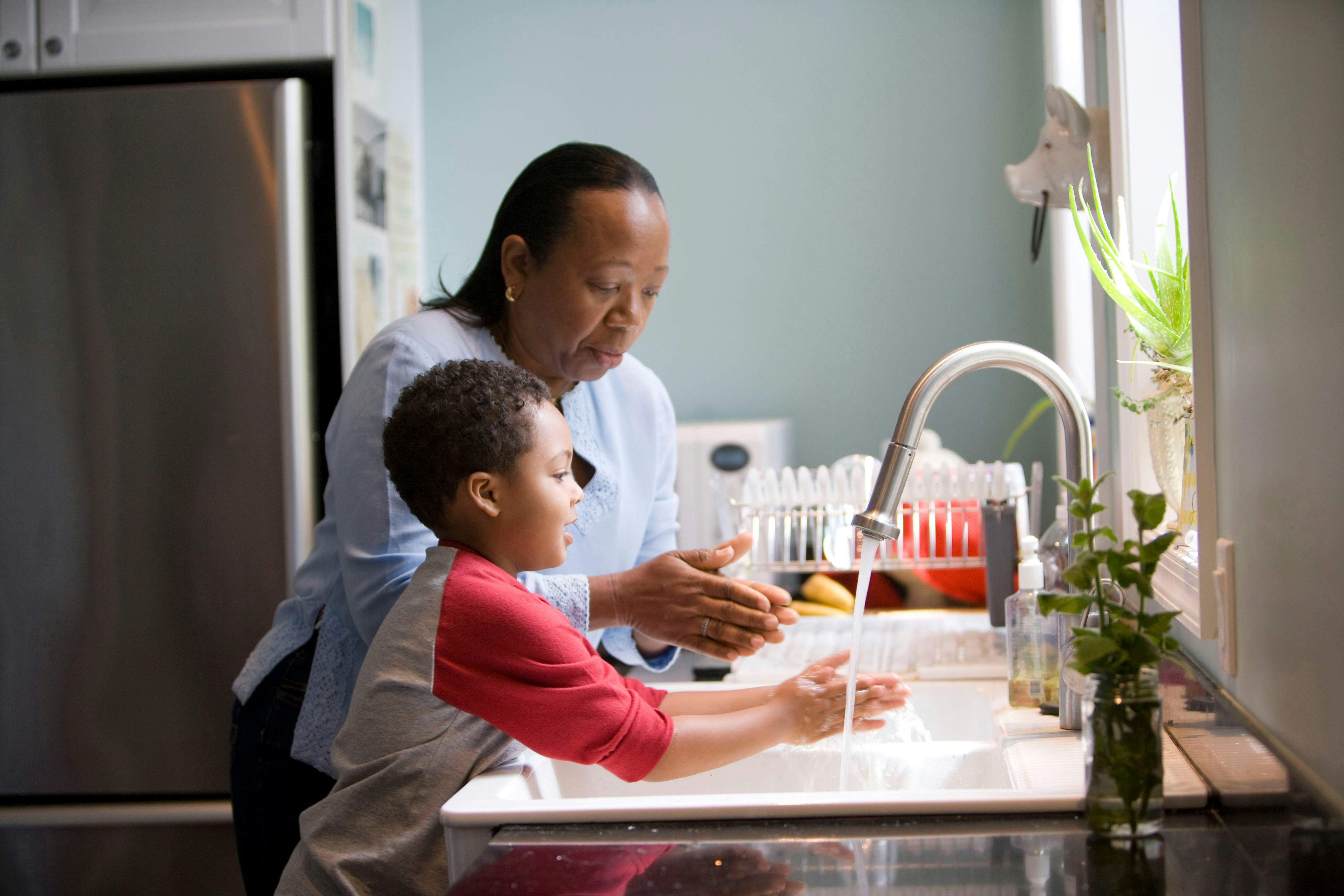 A caregiver helping a child wash their hands at the kitchen sink